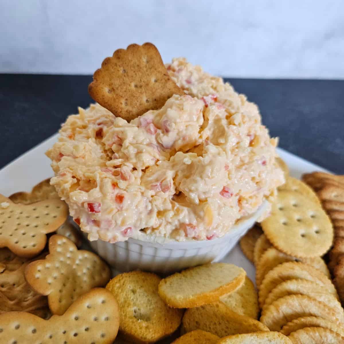 Pimento cheese in a white bowl on a plate with crackers