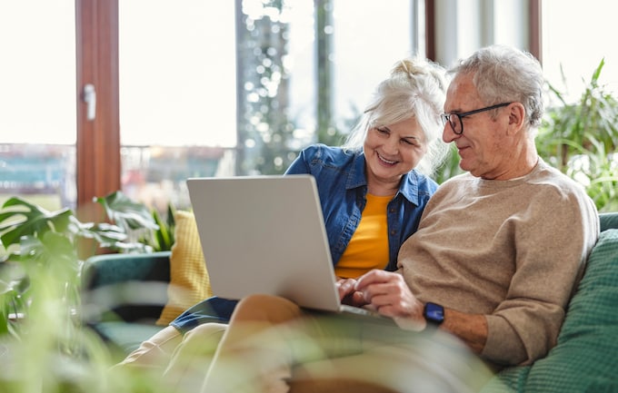 senior couple sat on couch with laptop wondering how long does equity release take