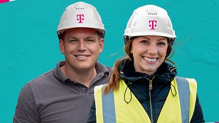 Zwei Personen mit Arbeitskleidung und magenta-farbenen Bauarbeiter-Helm