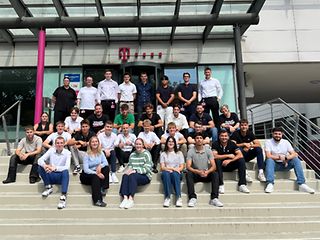 Gruppenbild mit ca. 30 jungen Menschen auf der Eingangstreppe zu einem Telekomgebäude.