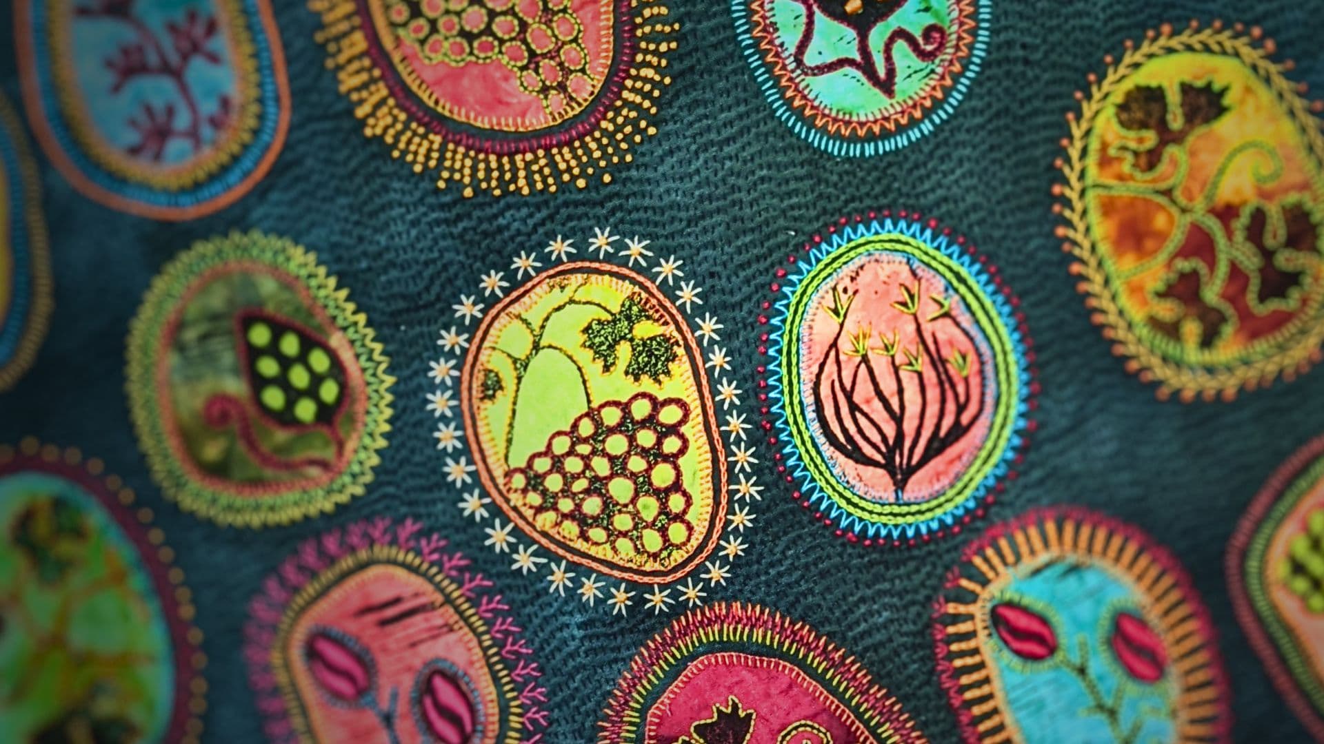 A close up of a stitched artwork with lino-printed motifs in bright colours on a teal background.