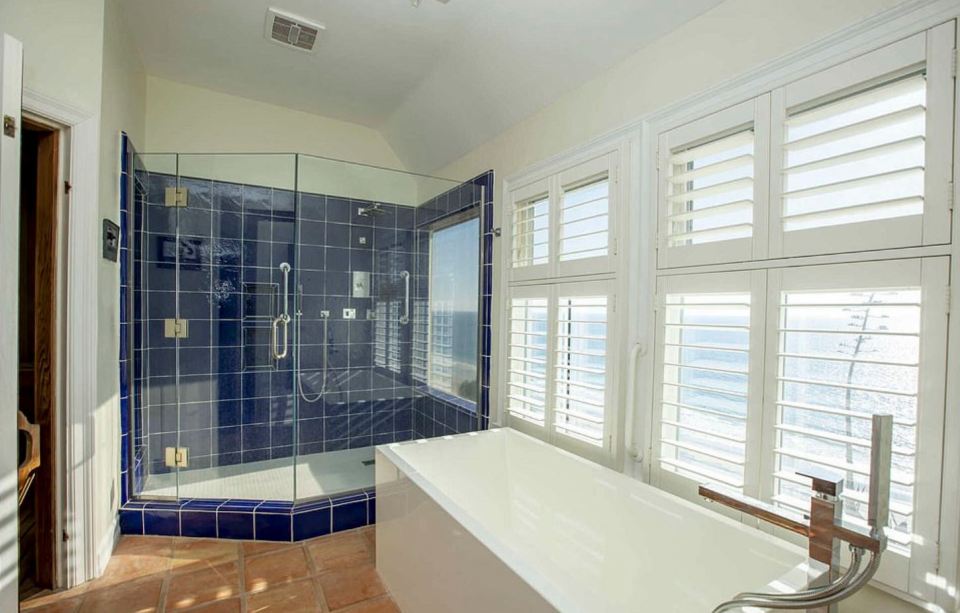  The master bathroom has a large blue-tiled shower with a modern tub and a sauna