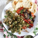 overhead shot of herb tofu skewers with chimichurri sauce, grilled vegetables, rice and naan bread