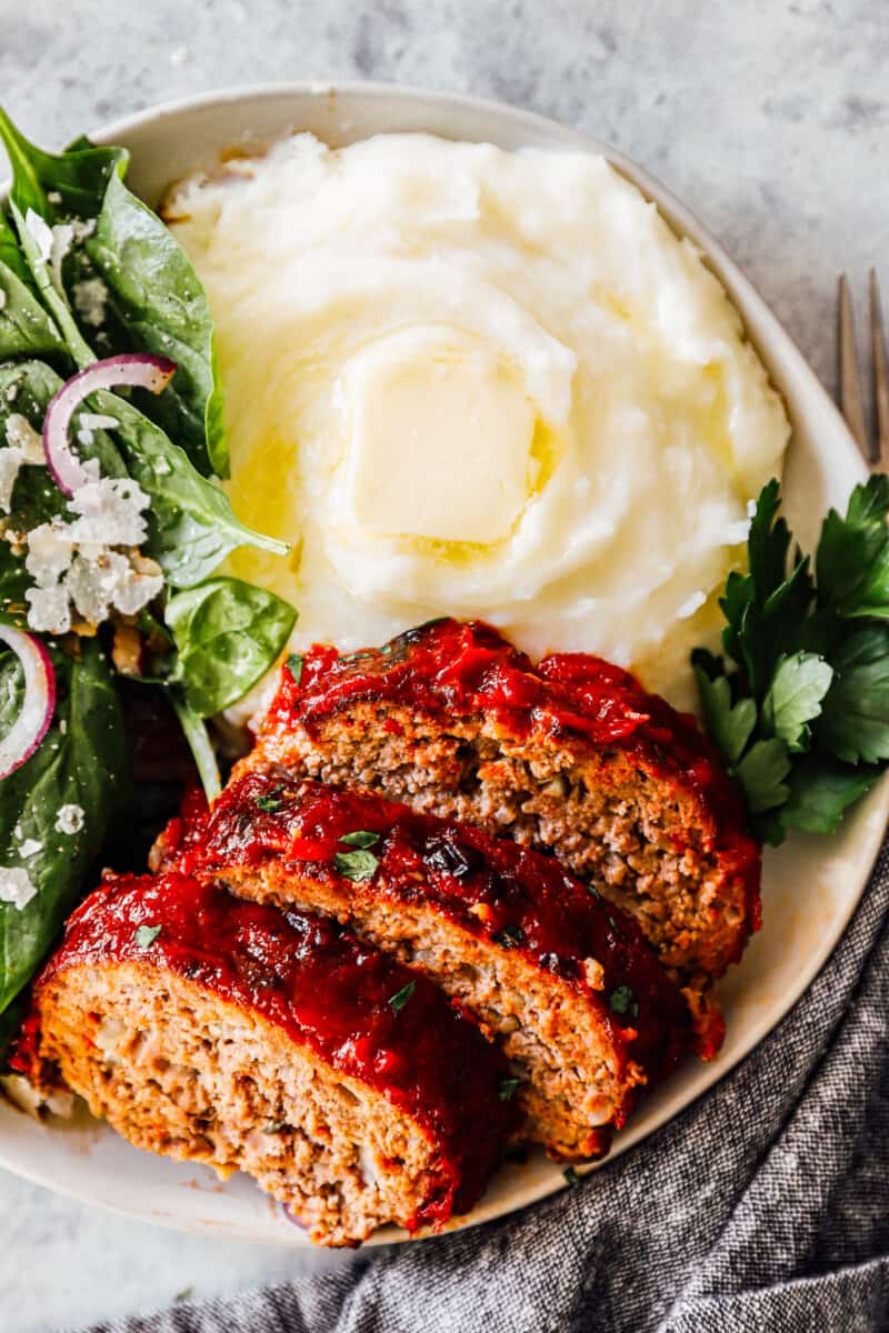 slices of air fryer meatloaf on plate with mashed potatoes and salad