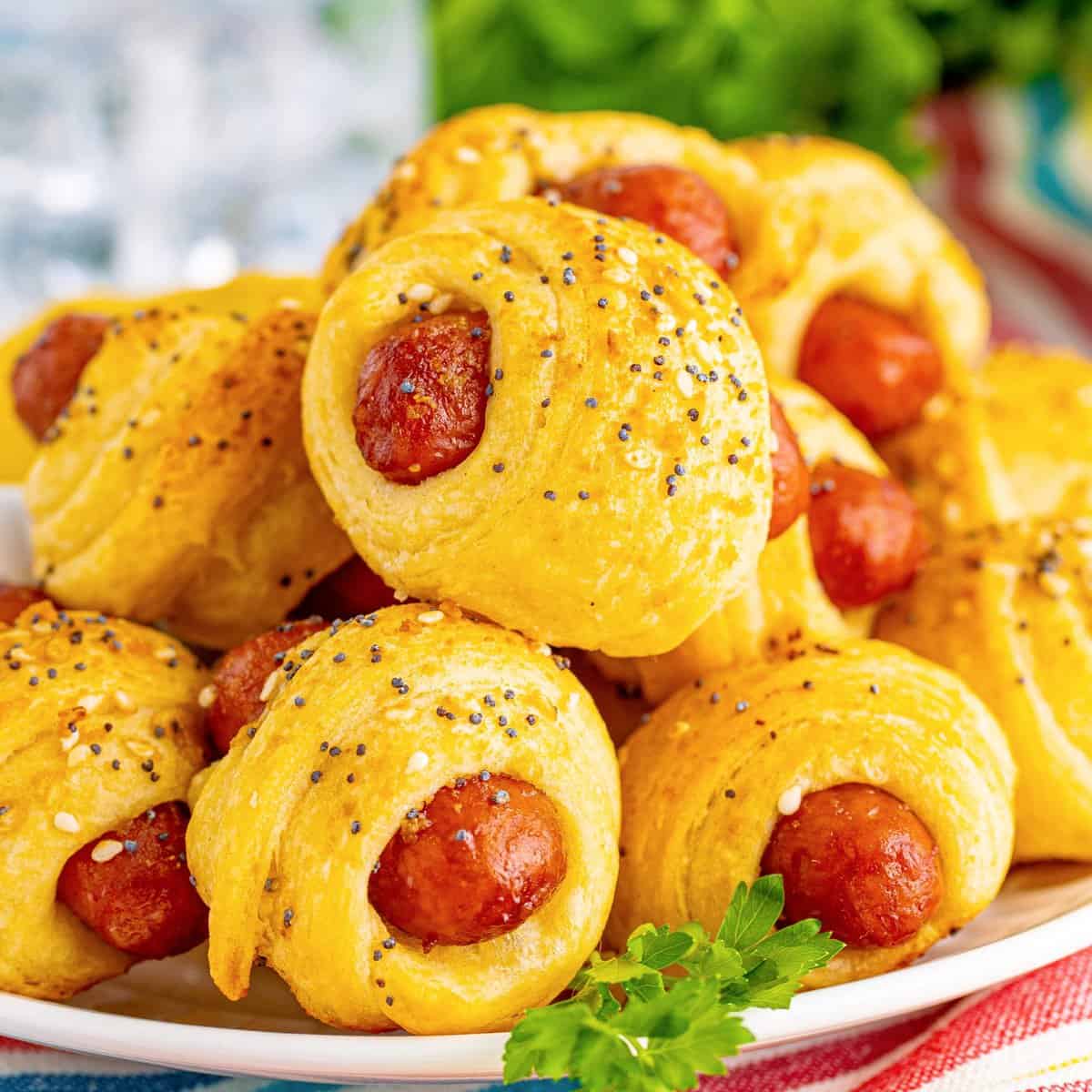 Square image close up of stacked Glazed Pigs in a Blanket on white plate.