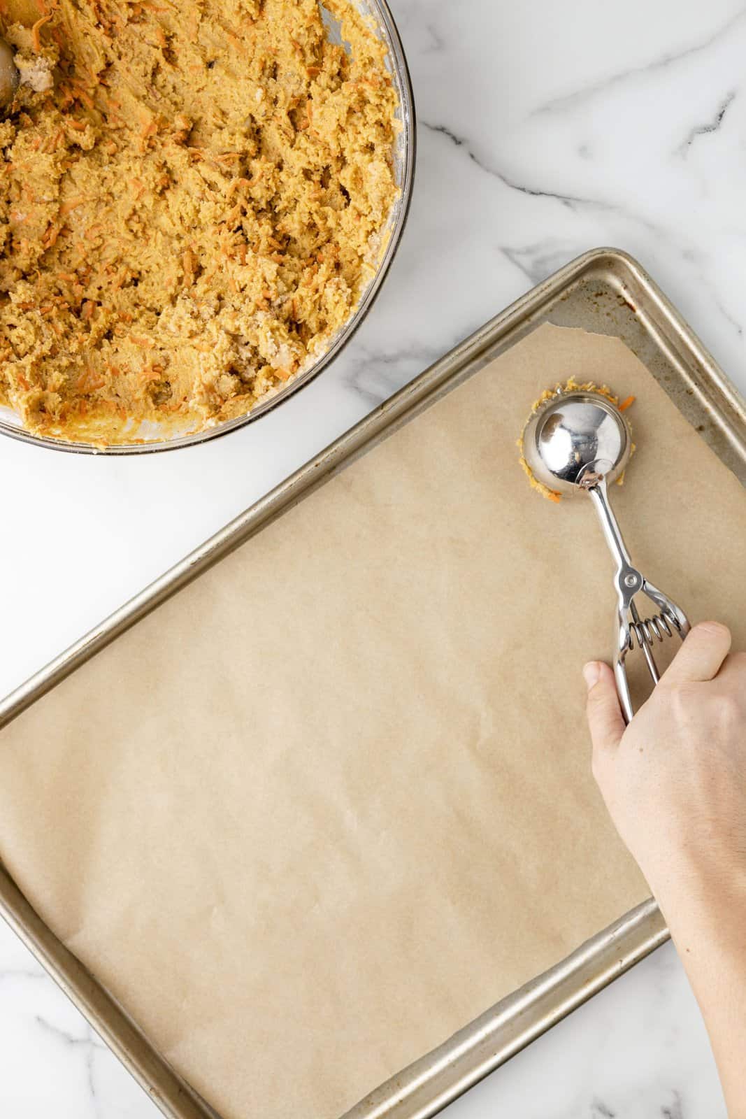 Cookie scooper laying cookies on a parchment paper lined baking tray.