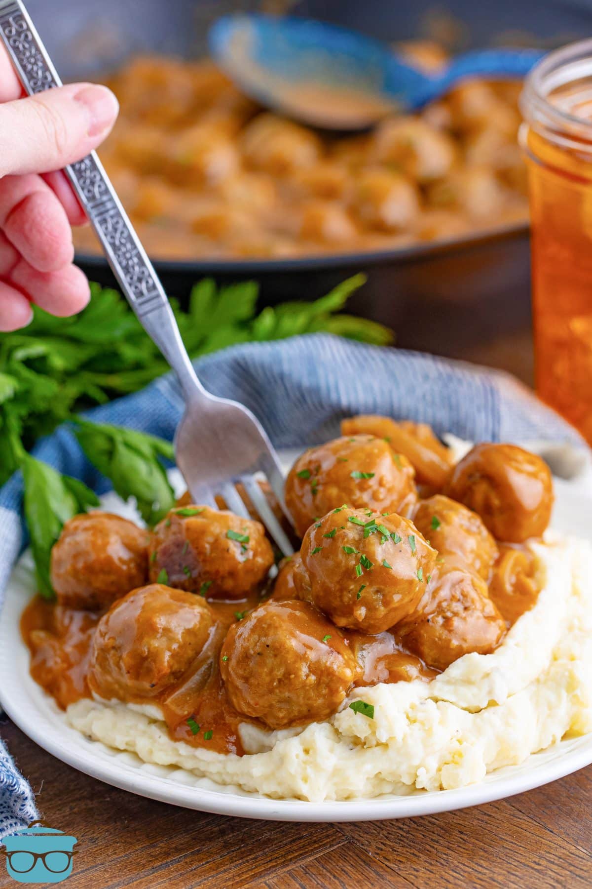 A hand using a fork to get some Salisbury Steak Meatballs from the plate full.