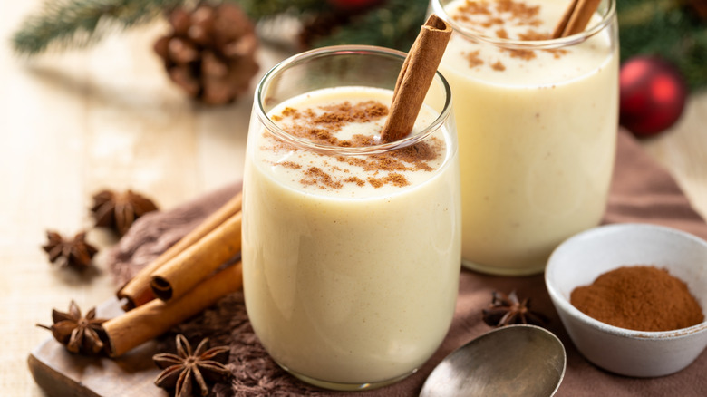 Two glasses of eggnog surrounded by cinnamon sticks