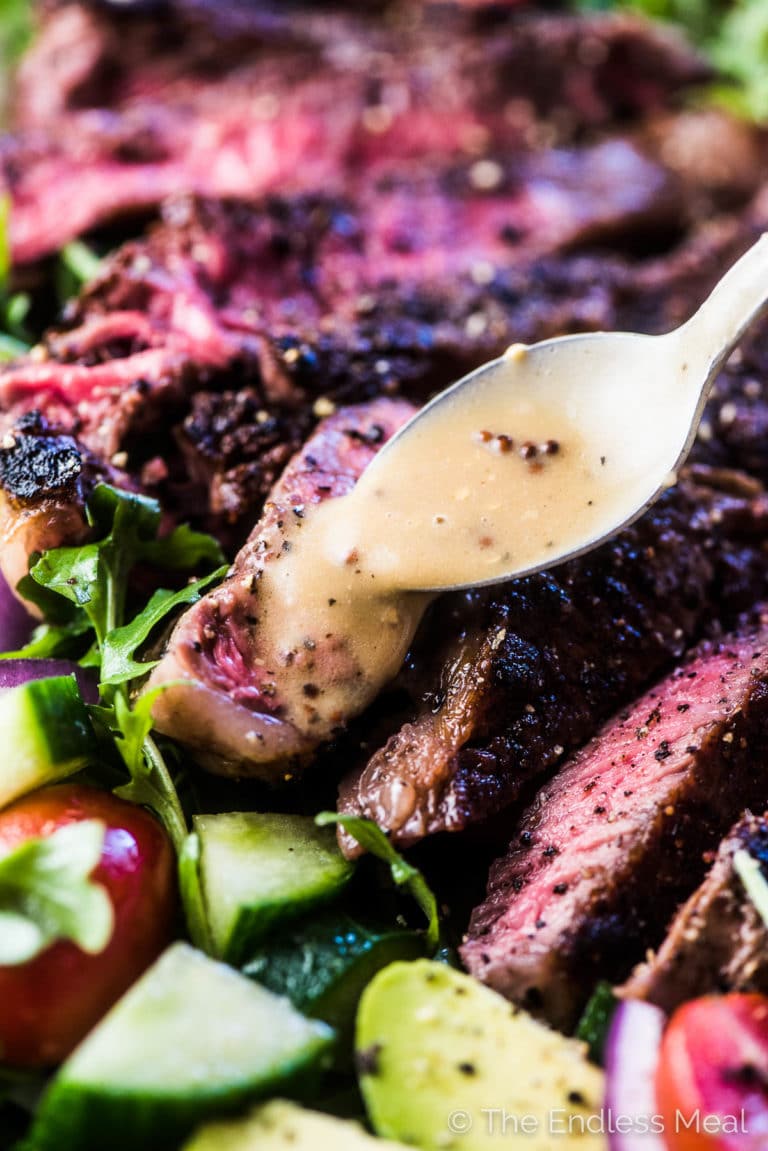 A close up of the salad dressing being poured over the steak salad.