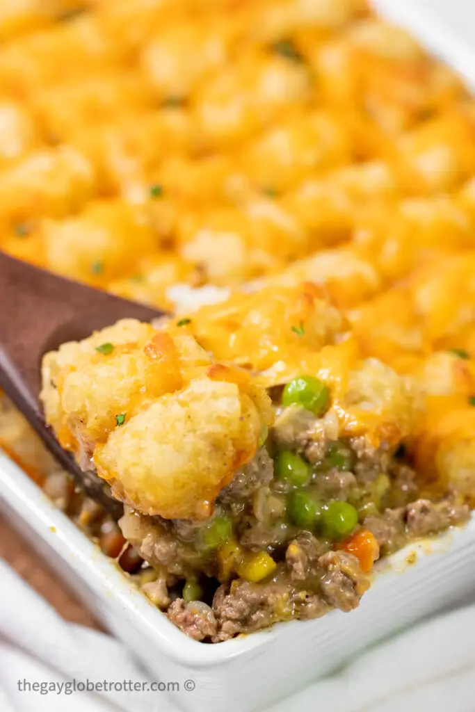 A serving spoon scooping tater tot casserole.