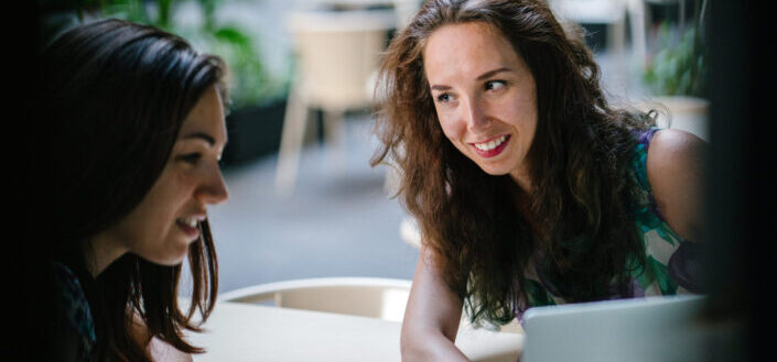 Two talking women while using laptop