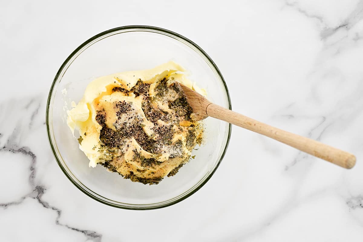 A wooden spoon, butter and spices in a glass bowl.