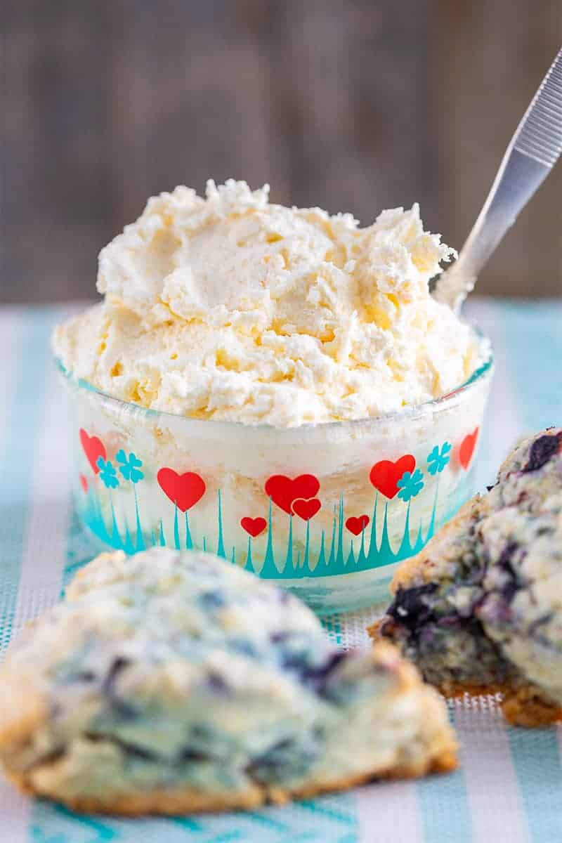 close up clotted cream in a heart patterned Pyrex container and blueberry scones