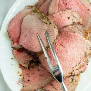 thin slices of stuffed eye of round roast in a white plate with pot fork