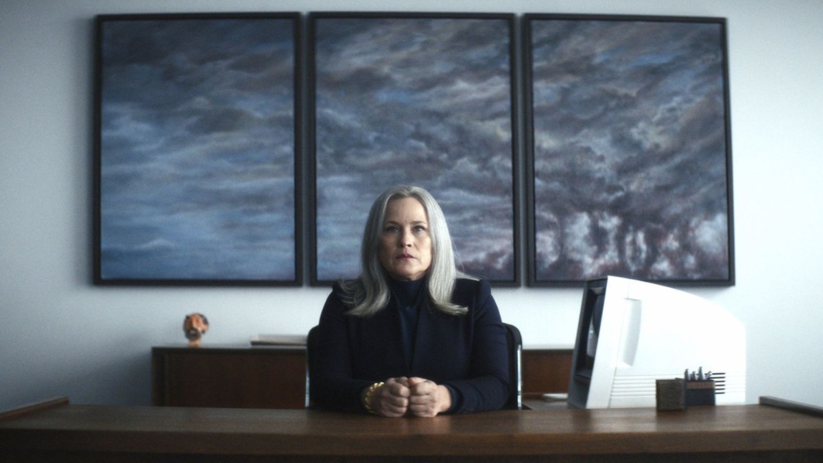 In Severance, Patricia Arquette as Harmony Cobel sits at her desk surrounded by muted dark colors