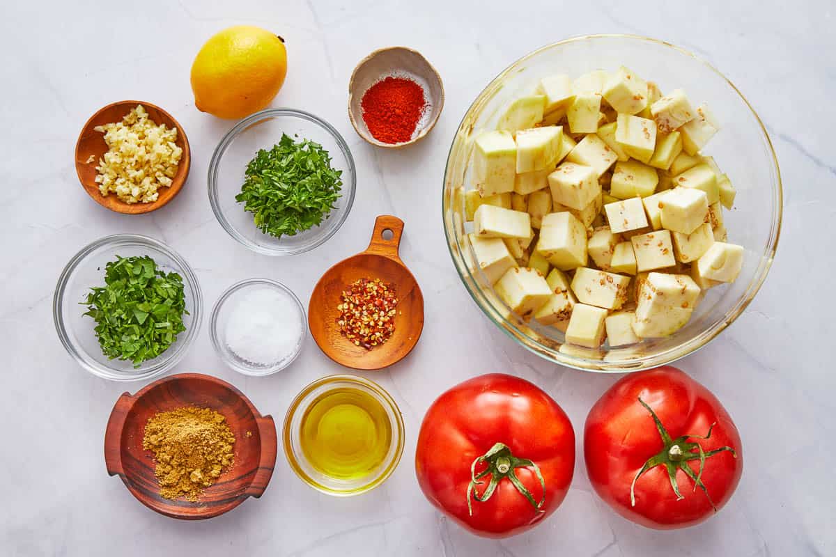 Ingredients for how to make zaalouk with eggplant, tomatoes, fresh cilantro, parsley, garlic, spices and lemon juice