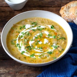 soupe jo in a bowl garnished with half and half and chopped parsley, surrounded by small bowls of olive oil, chopped parsley and half and half, and slices of crusty bread.