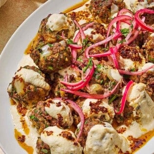 The turkish meatballs and yogurt sauce topped with pickled red onions and chopped parsley on a platter next to a bowl pickled red onions.