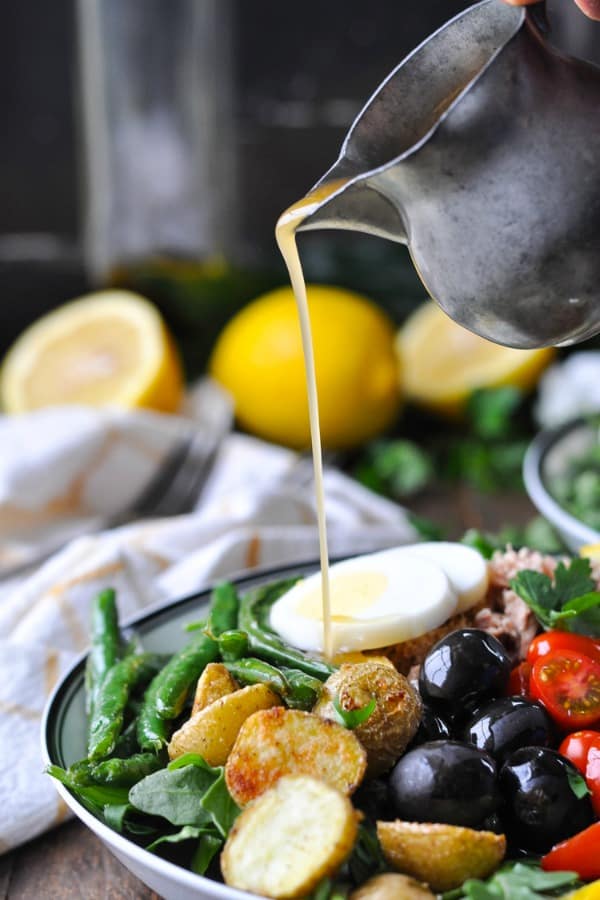 Pouring homemade vinaigrette over a Tuna Nicoise Salad