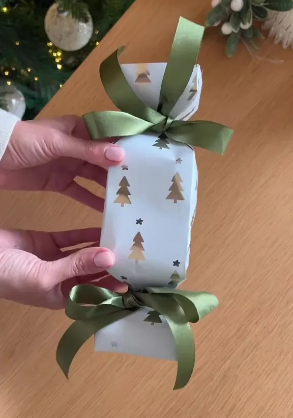 Christmas cracker with a green ribbon and gold Christmas trees.