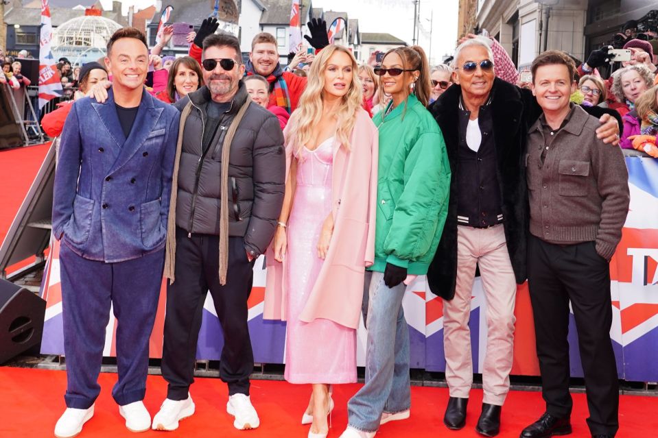 The judges of The X Factor posing on a red carpet.