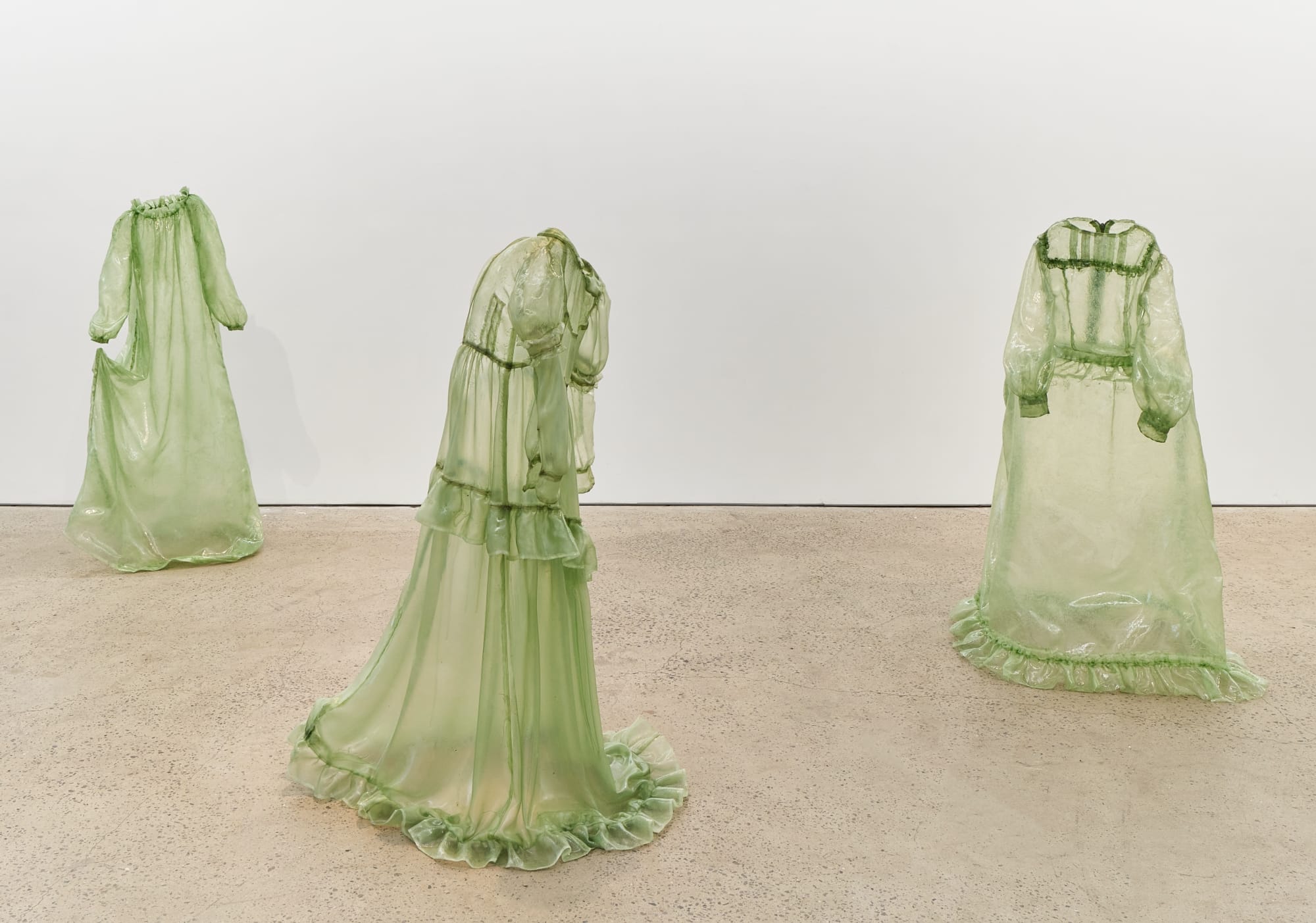 a collection of stiff green fiberglass victorian style dresses standing without wearers in the middle of a gallery