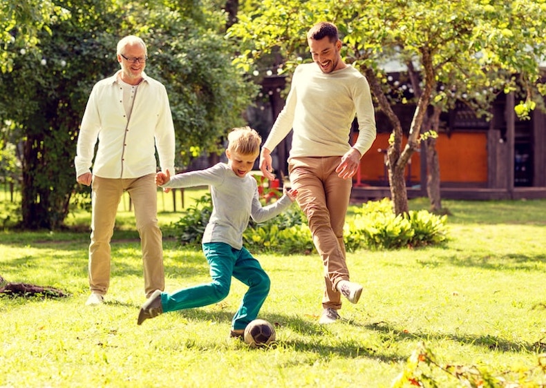 child playing football in the garden with father and grandfather