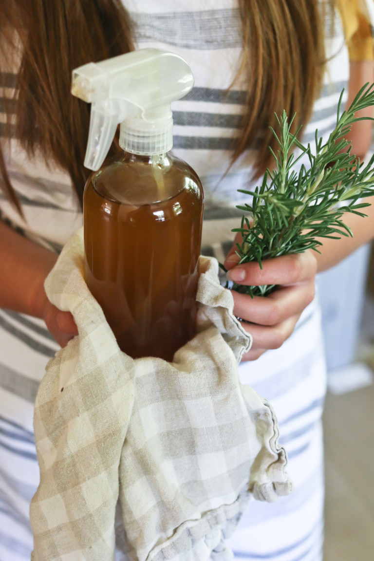 Someone holds a glass spray bottle of homemade rosemary hair water