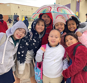 Group of students outside in the rain under an umbrella