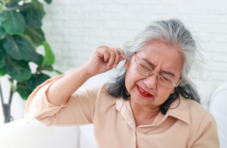 The senior woman indicates a possible earache by holding her ear