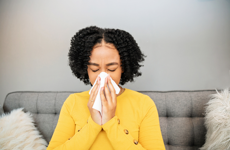 A woman with sinusitis blowing her nose on a couch