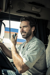 Smiling truck driver holding a CB radio microphone in truck cabin