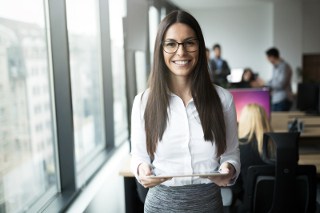 Businesswoman holding tablet in office with colleagues in background.