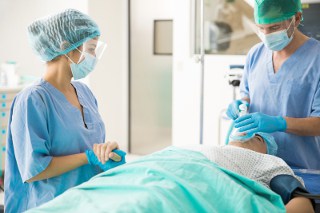 Two surgeons in scrubs and masks performing a medical procedure on a patient in an operating room.