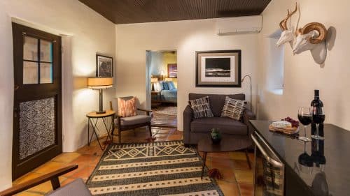 Sitting area in suite with wine fridge, tv, and two tables with chairs, decorated in modern Southwest style.