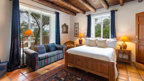 Bedroom with Saltillo tile floor, blue drapes on expansive windows, bed made up in white and southwestern-style sofa.