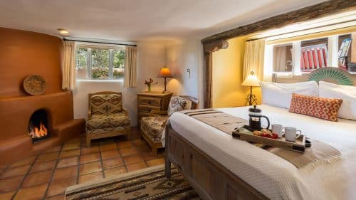 Plaster fireplace in bedroom with Saltillo tile floor, seating area and king-size bed inset cleverly into the wall.