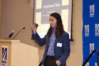 A young man gestures toward a laptop while another young man types on it as another young man looks on in a building lobby.