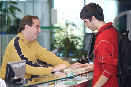 Un bibliothèque, au comptoir, fournit des informations à un étudiant