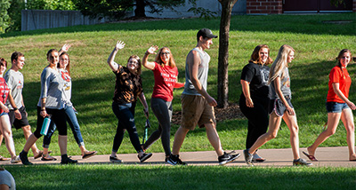 Three students wave to camera as they walk by