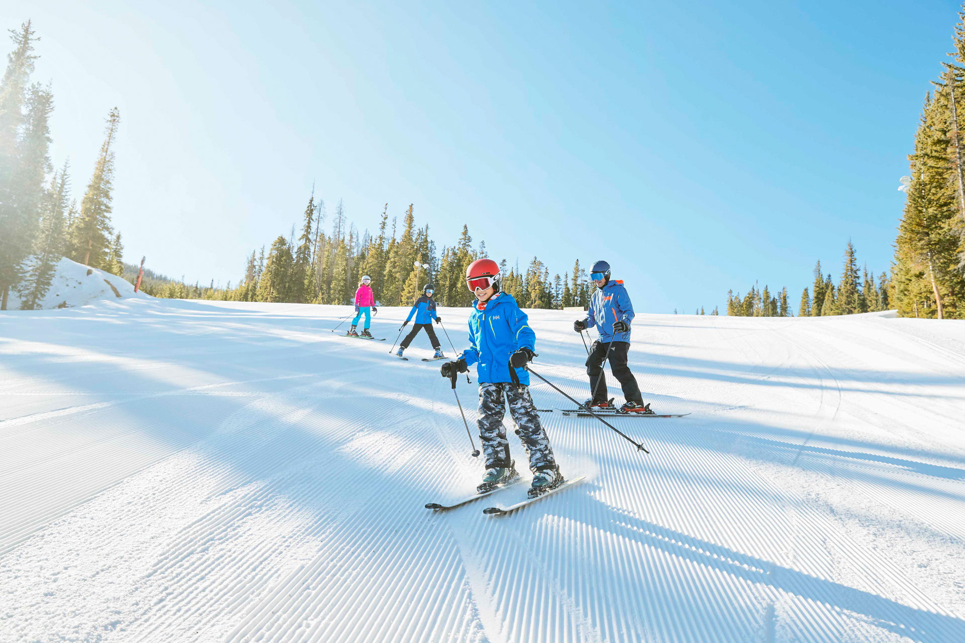 Family of four skiing down a groomed run at Keystone on a sunny day