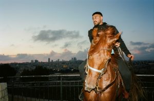 A man rides a horse against the setting sun in Palestine.