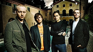 boy band group stands near brown house while taking photo