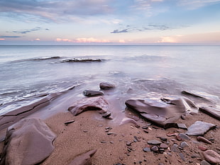 stone on sand beside seaside under cloudy blue sky during daytime