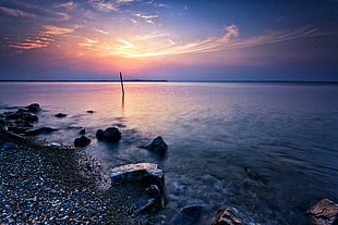 calm sea with stones on seashore under blue sky