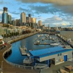 The Seattle foreshore including The City of Seattle, The Seattle Great Wheel, Lumen Field, the Bell Harbor Marina and Puget Sound.