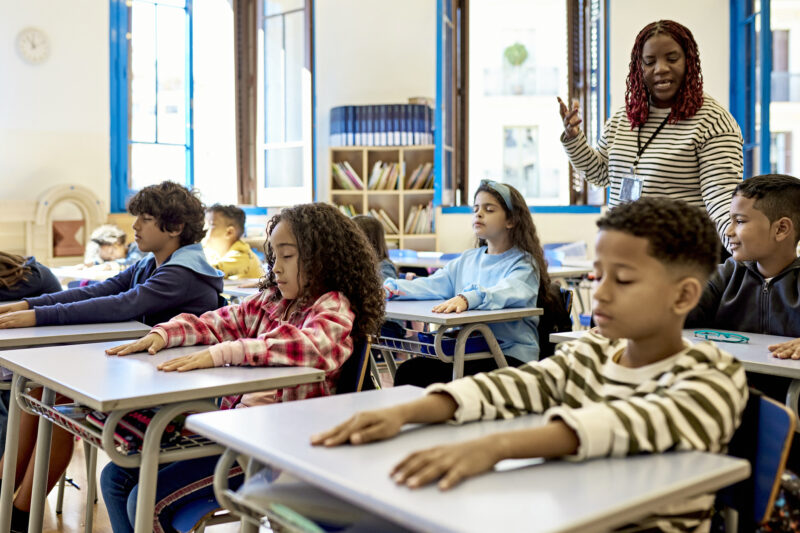 Front view of elementary age schoolchildren sitting at their child-size desks with arms relaxed and eyes closed, enjoying a break from studies.