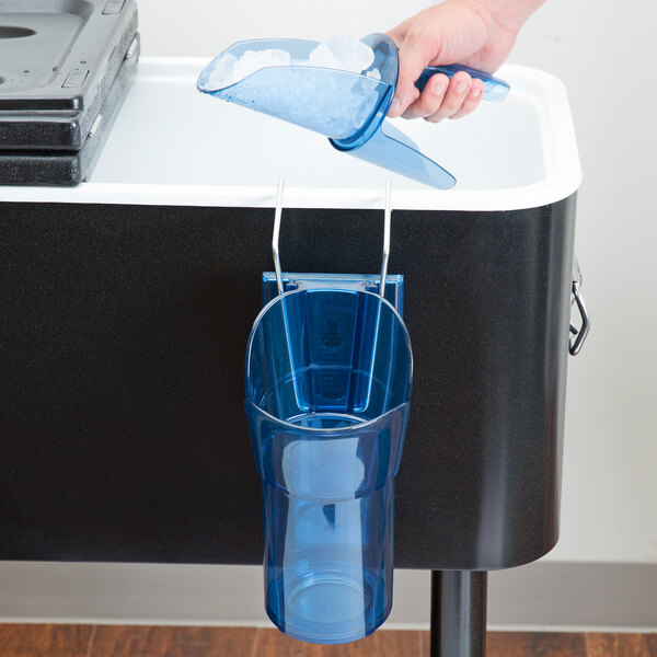 A hand holding a San Jamar ice scoop with ice over a blue plastic cup with a lid.