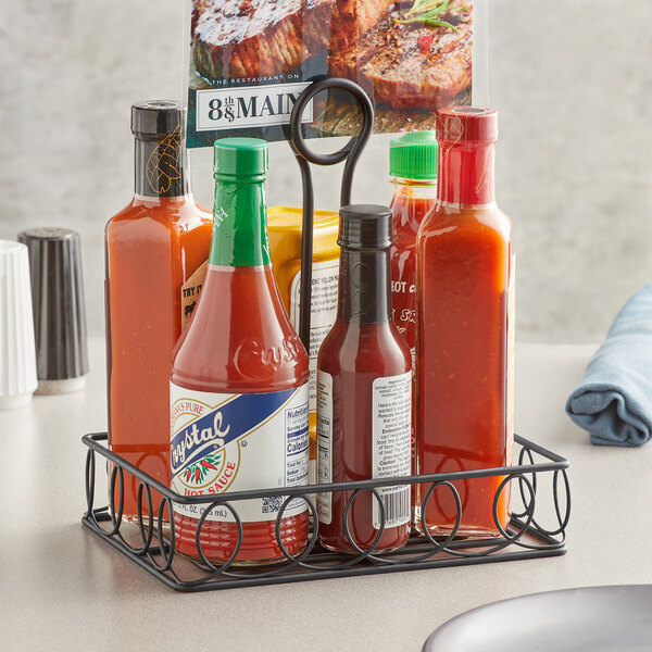 A black wrought iron rectangular condiment caddy holding a bottle of hot sauce and a bottle of mustard with a card holder.