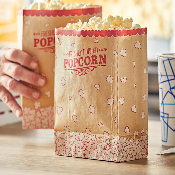 A close-up of two hands holding brown Carnival King popcorn bags with red and white designs.